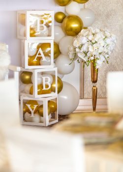 Vertical shot baby gender reveal party decorations with boxes with white and gold balloons